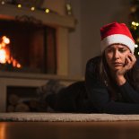 Article thumbnail: Young woman laying on carpet alone at home around fireplace and Christmas decoration on background.