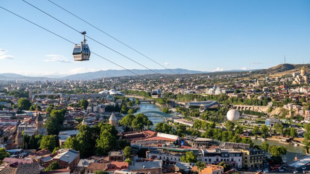 Article thumbnail: Aerial view of Tbilisi, capital city of Georgia. A cable car in foreground. Summer cityscape with Kura river, Peace bridge, Tbilisi cathedral, and Music Theatre Exhibition Hall building.